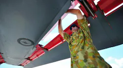 A technician wearing military fatigues standing under the wing of an airplane