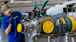 A technician wearing a blue polo working on an airplane engine, with the word 'BLACKHAWK' printed at the top of the photograph