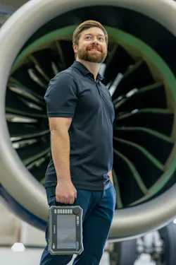 A man holding a tablet-based tool standing in front of an airplane engine